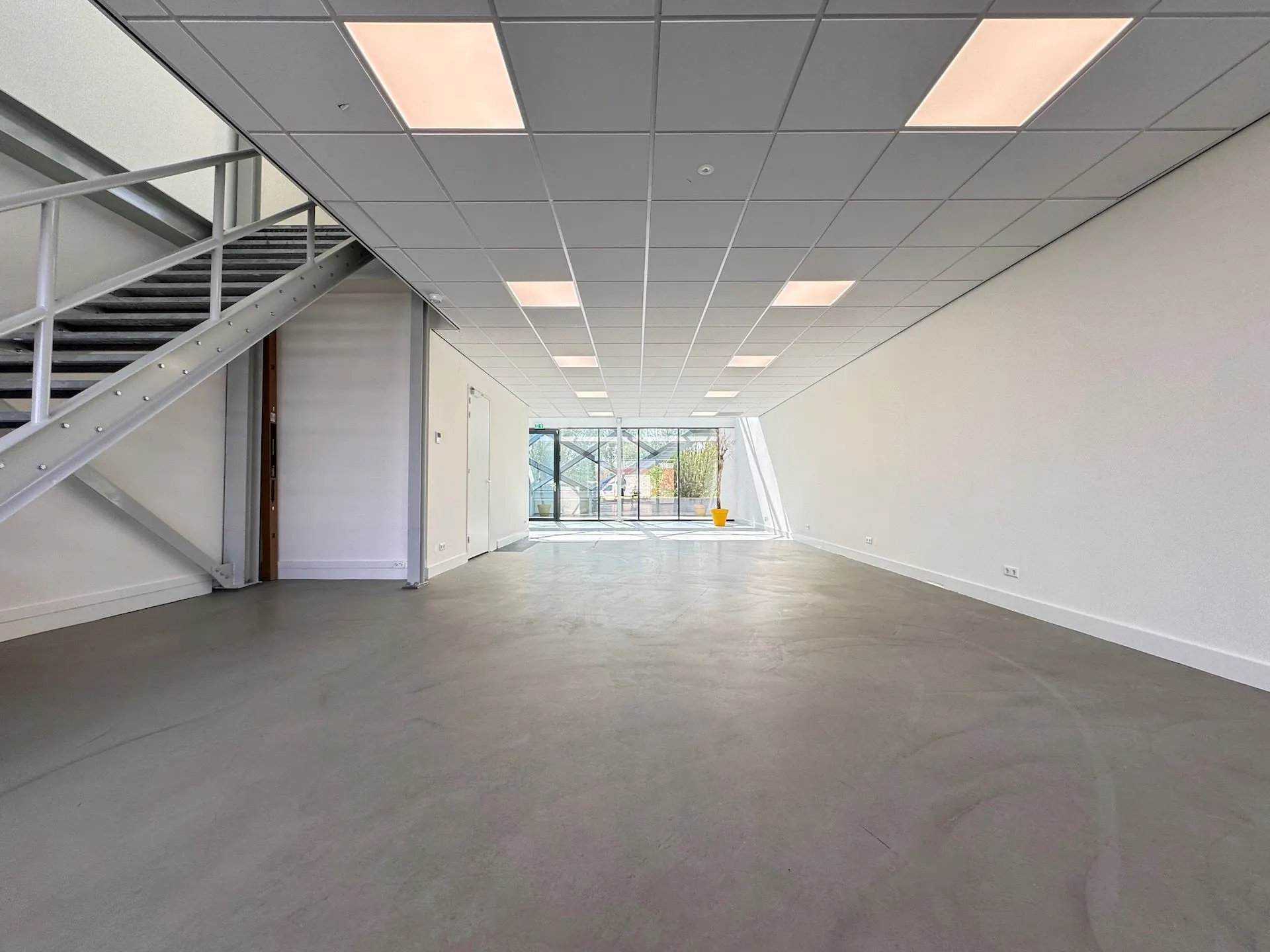 Leeg bedrijfs- of kantoorruimte in het Mart Stamhof met een betonnen vloer, systeemplafond en trap naar boven.